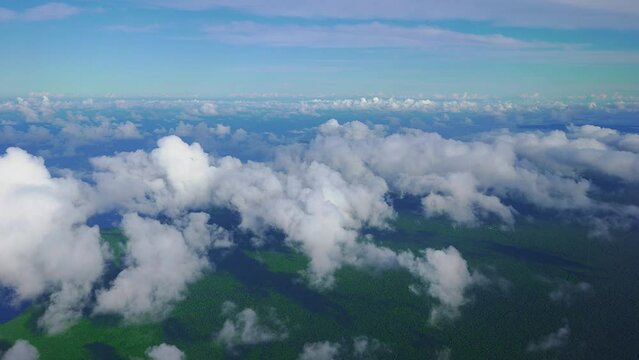 A beautiful scene of clouds and a forested coast as seen from the window of a plane in daylight.