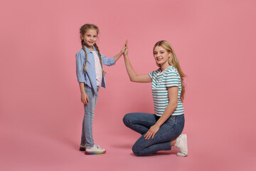 Mother and daughter giving high five on pink background