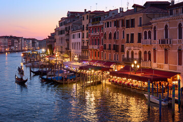 Obraz na płótnie Canvas Amazing view from the Rialto Bridge in Venice, Italy. Colorful cityscape with picturesque facades of old buildings and gondolas under cloudless sunset sky.