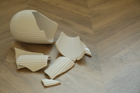 Broken white ceramic vase on wooden floor. Space for text