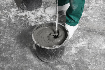 Worker mixing concrete in bucket indoors, closeup