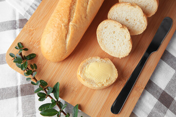 Cut baguette with fresh butter on checkered tablecloth, top view