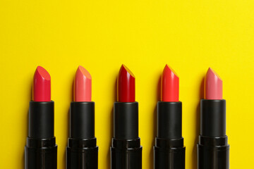 Many bright lipsticks on yellow background, flat lay. Space for text