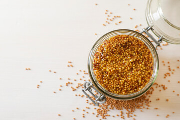 Jar of whole grain mustard on white wooden table, top view. Space for text