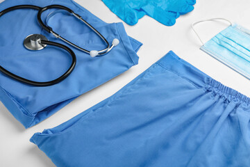Medical uniform, stethoscope, face mask and rubber gloves on white background, closeup view