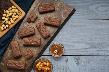 Fototapeta na wymiar Delicious chocolate candy bars with caramel and nuts on grey wooden table, flat lay. Space for text