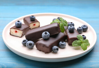 Delicious glazed curd snacks with fresh blueberries and mint on light blue wooden table