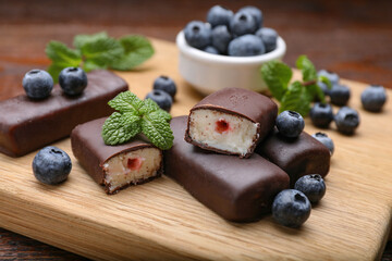Delicious glazed curd snacks with blueberries on wooden table, closeup