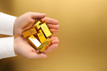 Man holding shiny gold bars on color background, top view. Space for text