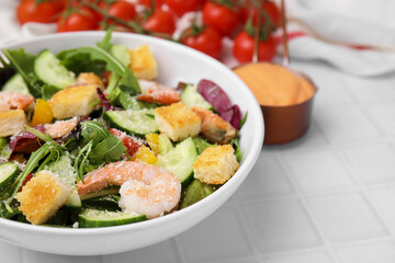 Delicious salad with croutons, cucumber and shrimp served on white tiled table, closeup. Space for text