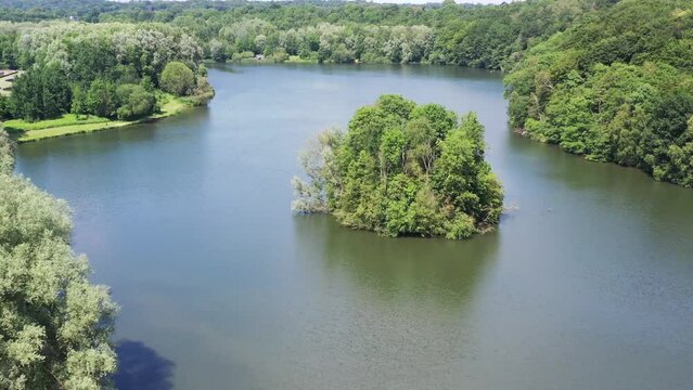 Peaceful flight over a calm serene lake surrounded by a forest of trees on a clear sunny day in spring