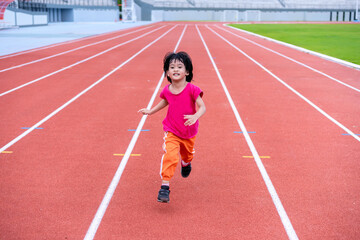 Fototapeta premium A girl in a pink sportswear and sneakers runs on the running track at the stadium outdoors.