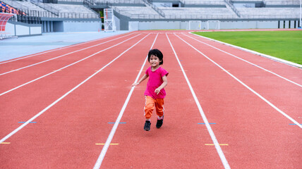 A girl in a pink sportswear and sneakers runs on the running track at the stadium outdoors.