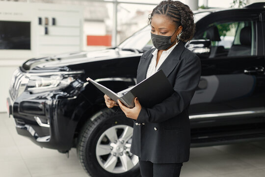 Black saleswoman standing at auto showroom and wearing a face mask