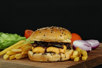 Hamburger with caramelized onion, cheese and french fries, with lettuce, tomato and red onion in the background