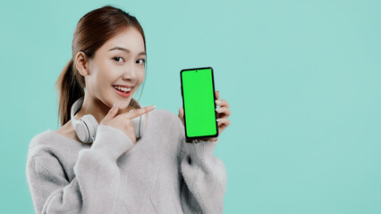 Pretty Asian student girl show blank green screen of mobile telephone and point finger isolated on...
