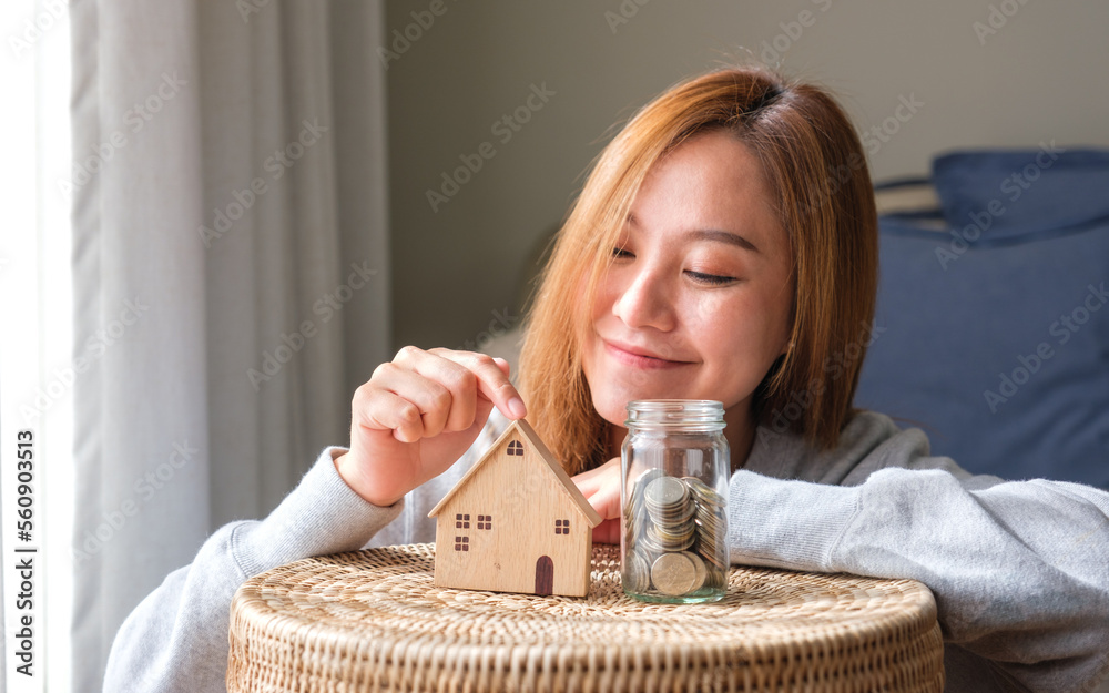 Wall mural Portrait image of a woman with a wooden house models and a glass jar of coins for saving money concept