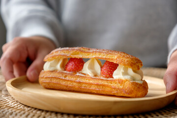 Closeup image of a woman holding a plate of strawberry Eclair
