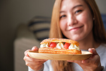 Portrait image of a woman holding a plate of strawberry Eclair