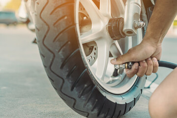 Hands of man check inflator pressure and inflates a tire on motorcycle with an air compressor. Man...