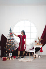 Portrait of a pretty young girl wearing a red gown, smiling at the camera, standing in decorated Christmas living room indoors