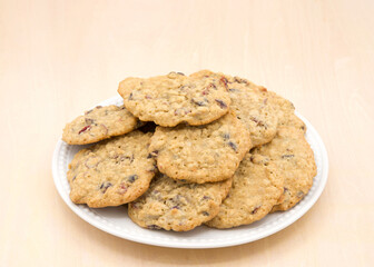 Close up on one porcelain plate full of Oatmeal Cranberry cookies on a light wood table background.