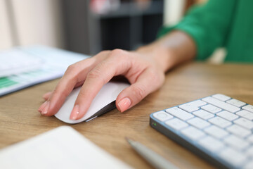 Close-up of business woman's hand holding computer mouse on office desk with keyboard and documents.