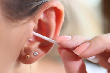 Close up of women cleans her ear with cotton swab.