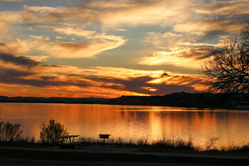 Obraz premium A beautiful golden sunset over a lake with shadows and relfections on the water located at Inks Lake State Park Burnet Texas USA Many families enjoy the park for camping and fishing.