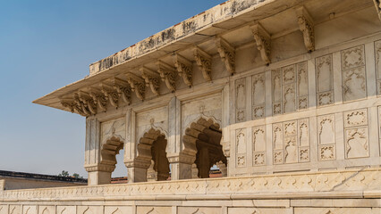Details of the architecture of the ancient Red Fort. The white marble Diwan-i-Khas building with arches, colonnades, elegant carvings on the walls against the blue sky. India. Agra