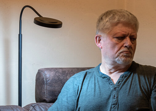 An elderly man sits lonely and sad in a room. He looks depressed. A lamp illuminates his face.