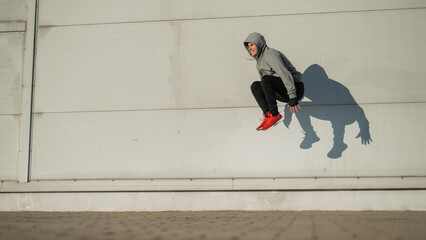 Caucasian man in hoodie jumping high with hands on knees outdoors. 