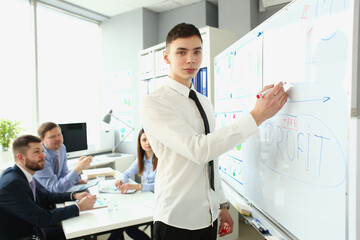 Young businessman stands near board with graphs and demonstrates statistics