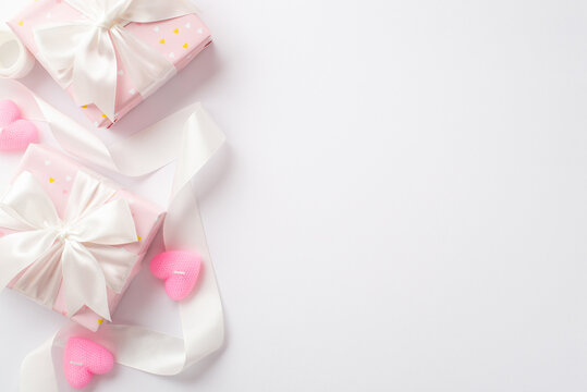 Valentine's Day concept. Top view photo of pastel pink gift boxes curly silk ribbon and heart shaped candles on isolated white background with copyspace