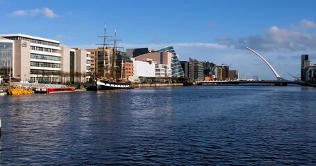 An over water  slow  zoom shot of the River Liffey in the evening sunshine, showing the North Wall  Quay with the Samuel Beckett Bridge in the distance