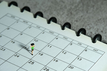 Miniature people toy figure photography. A boy running above monthly planner calendar. Grey cloudy...