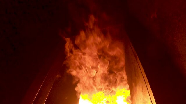 Fire flashover inside burn building of fire training center. Flames shoot up and roll along the ceiling toward the camera. Tilt up, tilt down.