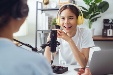 Young Asian woman use microphones wear headphones with laptop record podcast interview for radio....