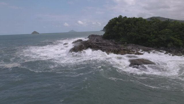 Orbital flight over an island with rock and trees in the acean, blue sky behind.