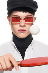 Cropped close-up shot of a young man wearing sunglasses with red lenses. A guy with rectangular sunglasses in a black cap is holding a table tennis racket on a white background. Front view.