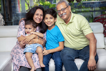 Portrait of Happy indian grand parents sitting with their grand children at home. Asian senior and young couple with kids looking at camera.