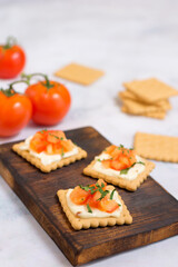 Quick cooked appetizer of cream cheese on a cracker with tomato and herbs on a wooden dark board and a light background