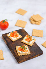 Quick cooked appetizer of cream cheese on a cracker with tomato and herbs on a wooden dark board and a light background