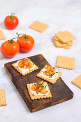 Quick cooked appetizer of cream cheese on a cracker with tomato and herbs on a wooden dark board and a light background