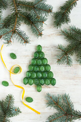 Top view of a green caramel Christmas tree decorated with fir branches on a light wooden background. Holiday atmosphere.