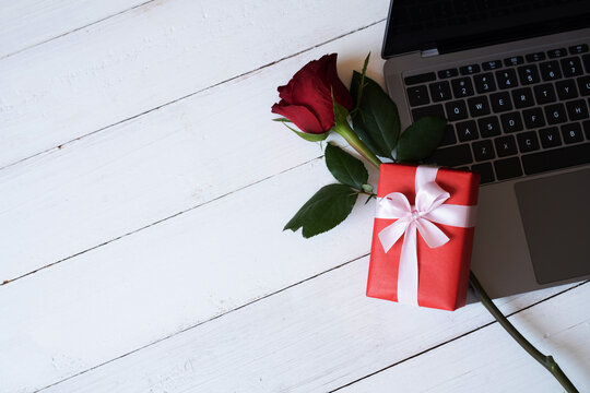 Red rose and red gift box with laptop on white wooden background with. Valentine's day, wedding, birthday and special occasion concept. Copy space for text. Top view, Flat lay.