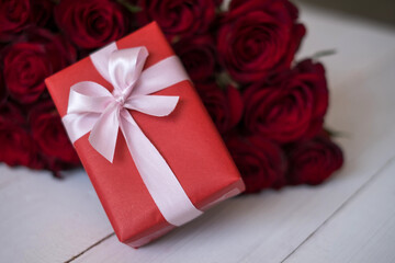 Close up red gift box with bunch of rosy roses blurred background. Valentine's day, wedding, birthday and special occasion concept. Copy space for text.