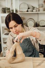 A beautiful young woman shaping a vase from clay in a pottery studio