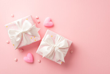 Valentine's Day concept. Top view photo of two gift boxes with white ribbon bows heart shaped candles and sprinkles on isolated pastel pink background