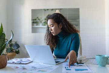 Focused Asian woman using laptop at home, looking at screen, chatting, reading or writing email, sitting on couch, female student doing homework, working on research project online